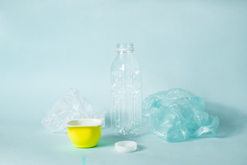 Disposable plastic items of every day use on blue background. Concept of ecological footprint of human: plastic bottle cap and food packaging that don't get recycled