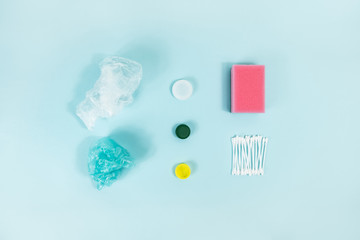 Disposable plastic items of every day use on blue background, top view. Concept of ecological footprint of human: plastic bottle cap, personal hygiene items and food packaging that don't get recycled