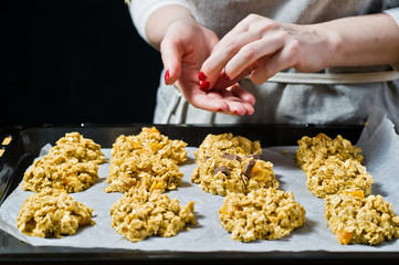 Female chef preparing oatmeal cookies, spread the dough on the trays. Side view, black background, kitchen.