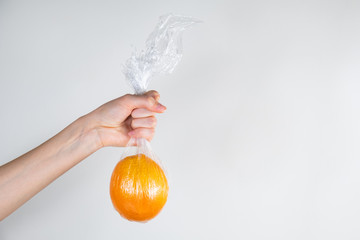 Excessive plastic use concept: orange in plastic wrap held in a hand. Unreasonably over-packaged...