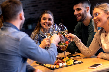 Group of young friends having fun in restaurant, talking and laughing while toasting with glass of wine.