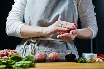 A female chef prepares Swedish meatballs from raw minced meat. Black background, side view, kitchen