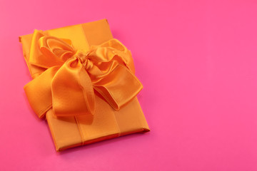 The gift is packed and decorated with a yellow bow on a pink background with copy space. Flat lay, top view. copy space