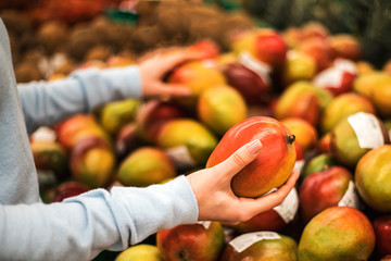 Young woman choose fresh mango at supermarket.