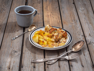 Nutritious breakfast of meatballs and fried potatoes, cut into large slices, tea in an aluminum gray mug for cutlery next to the plate