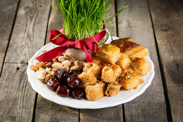 Nowruz holiday concept - grass, baklava sweets, nuts and seeds, copy space
