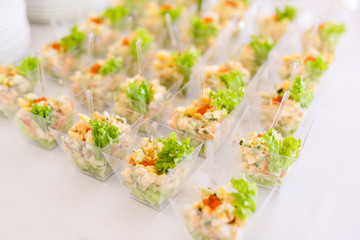 Little glasses with fresh salads, eggs, salmon and cucumbers standing on white table