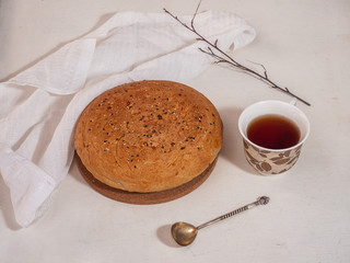 Homemade bread with flax and sesame seeds on a white table, a patterned cup and tea with a teaspoon