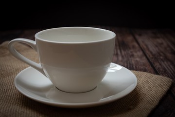 White cup of coffee and sackcloth on wooden table.