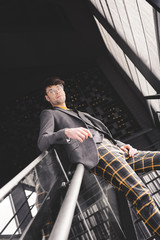 young stylish man in glasses posing on stairs and looking at camera