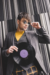 cheerful young man touching sunglasses and holding plastic retro vinyl record