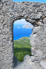 View of the coast through a window in the stone wall of the ruins of the Monolitos castle on the background of the coast, the island of Rhodes, Greece