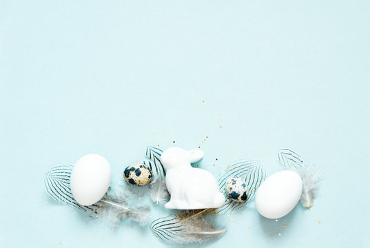 Easter composition with easter eggs, rabbit and feathers on blue background, space for text - Image