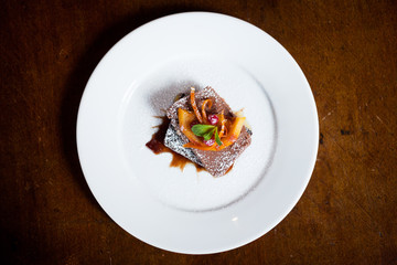birds eye view of chocolate dessert with icing sugar and orange garnish