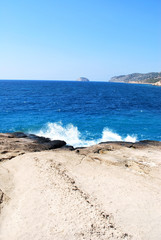 Large stones washed by sea waves with white foam against a blue sky, Cape Fourny, Rhodes Island, Greece