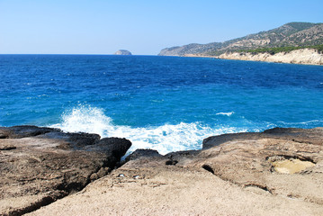 Large stones washed by sea waves with white foam against a blue sky, Cape Fourny, Rhodes Island, Greece