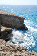 Close-up of large stones washed by sea waves with white foam against a blue sky, Cape Fourni, Rhodes Island, Greece