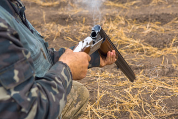 Hunter with a hat and a gun in search of prey in the steppe, reloads the weapon, the smoke from the...