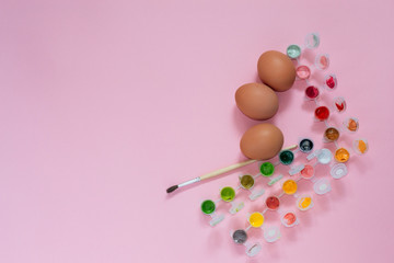 Chicken eggs decorating for Easter holiday. Closeup eggs, pallettes with paints, brush on pink background with copyspace.