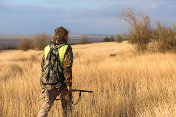 Hunter with a gun and a dog go on the first snow in the steppe, Hunting pheasant in a reflective vest	
