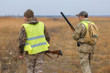 Hunter with a gun and a dog go on the first snow in the steppe, Hunting pheasant in a reflective vest	