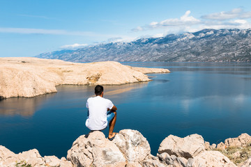 Junger Mann schaut auf eine Landschaft von Berge und Meer in Kroatien, Pag