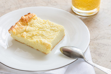 Piece of curd casserole on white plate and glass with smoothie on wooden saw cut.