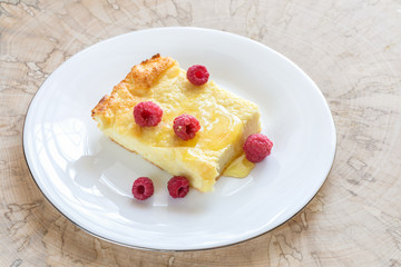 Piece of curd casserole with raspberries drizzled with honey on white plate on wooden cut. 