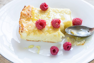 Close-up of piece of curd casserole with raspberries drizzled with honey and spoon on white plate. 