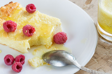 Close-up of curd casserole with raspberries, honey and spoon on white plate and glass with smoothie on wooden cut.