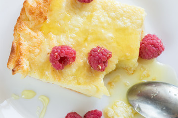 Close-up piece of casserole with raspberries with honey and metallic spoon on white plate. 