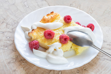 Curd casserole with raspberries, honey, sour cream and metallic spoon on white plate on wooden cut. 