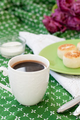Black coffee in a white sophisticated cup, delicious dietary cheesecakes from home-made farmer cheese for breakfast, a bouquet of purple tulips on a green tablecloth.