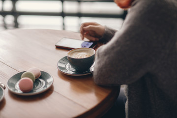 a cup of coffee, a hand with a telephone, a wooden table in a cafe. Because of the shoulder