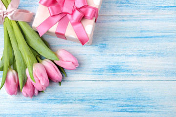 Bouquet of beautiful pink tulips flowers and gift box on a blue wooden table. Spring. holidays. place for text. view from above.