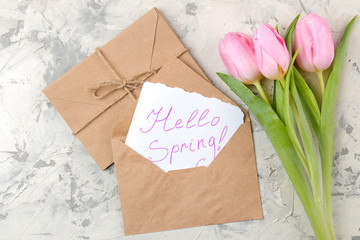 A bouquet of beautiful pink tulips flowers on a light concrete background. Spring. holidays. text hello spring on paper in an envelope. top view
