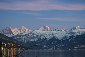 Fototapeta na wymiar Famous mountain range Eiger, Mönch and Jungfrau with snow on peaks at sunset reflecting in lake Thun..