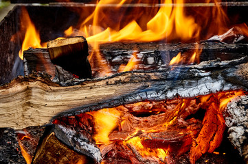 Burning wood in a barbecue for cooking meat in the heat of embers. Inside the coals glow red and orange fire. colors. Texture for design.