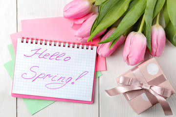 A bouquet of beautiful pink tulips flowers on a white wooden table. Spring. holidays. text hello spring on paper and gift box. top view