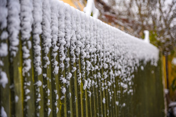 Green wooden fence with fresh covering of snow on the top. Shallow depth of field. Full frame.