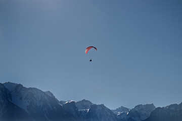 Paraglider tandem flying over alpine mountains.