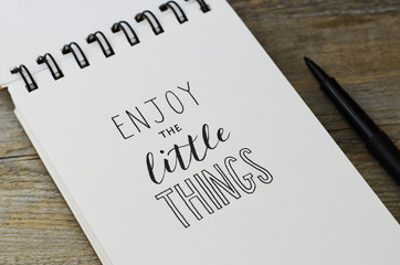 ENJOY THE LITTLE THINGS hand lettering in notebook with pen on wooden background