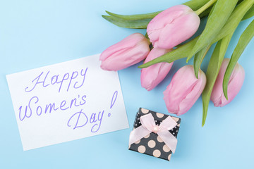 A bouquet of beautiful pink tulips flowers and a gift box on a trendy bright blue background. Spring. holidays. text happy women's day. view from above.