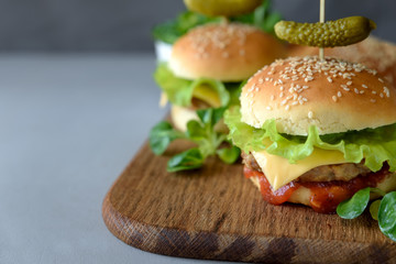Tasty homemade burgers with lettuce, ketchup, cheese and chicken on gray wooden background. Copy space