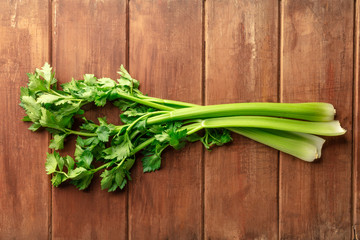 A photo of fresh organic celery leaves and stalks, shot from the top on a dark rustic wooden background