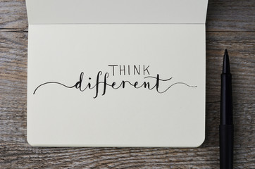THINK DIFFERENT hand lettering in notebook with pen on wooden background