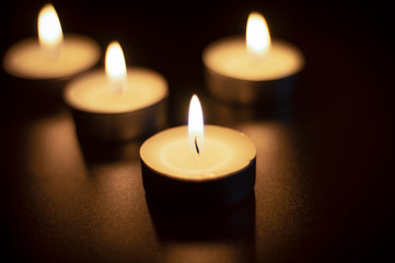 Fototapeta na wymiar Four tea candles with reflection on black