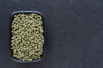 Dry green mung beans in a black  bowl on stone background