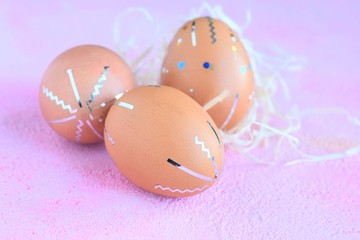 Beautiful decorated easter egg with blue paint spots and abstract shiny strips with natural straw on pink plaster background. Easter card with traditional eggs with colorful homemade decor 