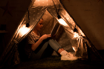 Kid using laptop while sitting in wigwam in dark room © LIGHTFIELD STUDIOS